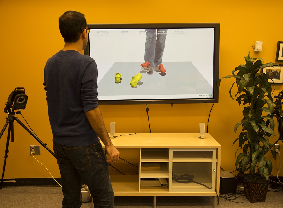 A person faces a large display showing a shared virtual dance floor with two pairs of rendered 3D feet.