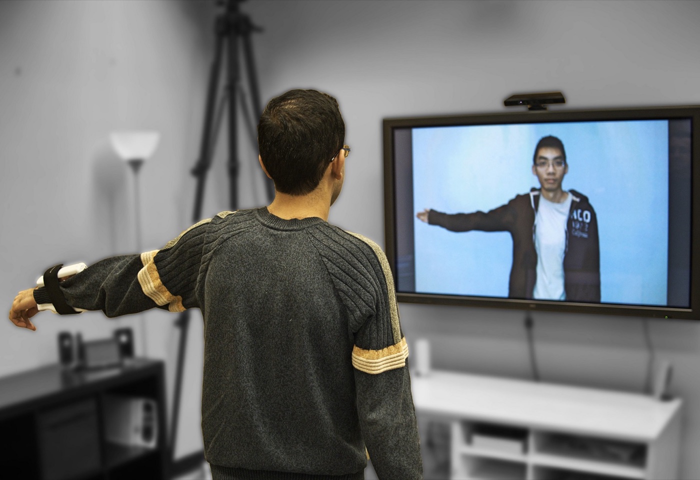 A person wearing a wrist-mounted haptic device stretches an arm toward a screen showing their remote exercise partner.